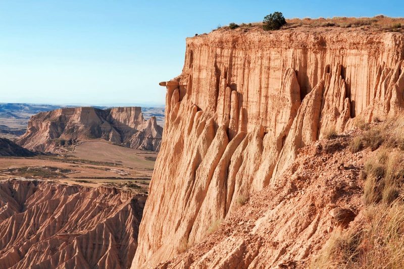 Falaises ocres sculptées par l'érosion dans le désert des Bardenas Reales, en Espagne, sous un ciel bleu clair.