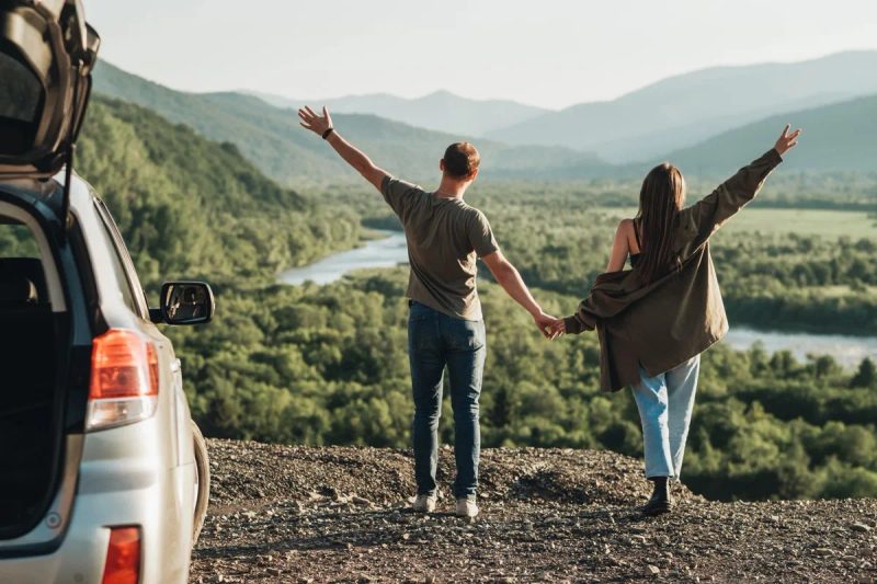 Couple profitant d'une vue panoramique sur les montagnes lors d'un road trip en voiture pas cher