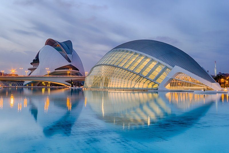 Vue nocturne de la Cité des Arts et des Sciences à Valence, montrant des bâtiments modernes en verre et métal se reflétant dans l