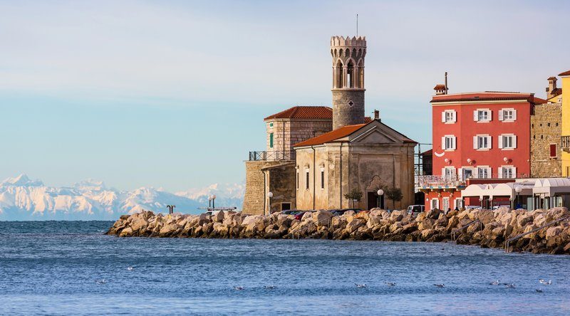 Phare et église au bord de mer à Piran avec les Alpes enneigées en arrière-plan