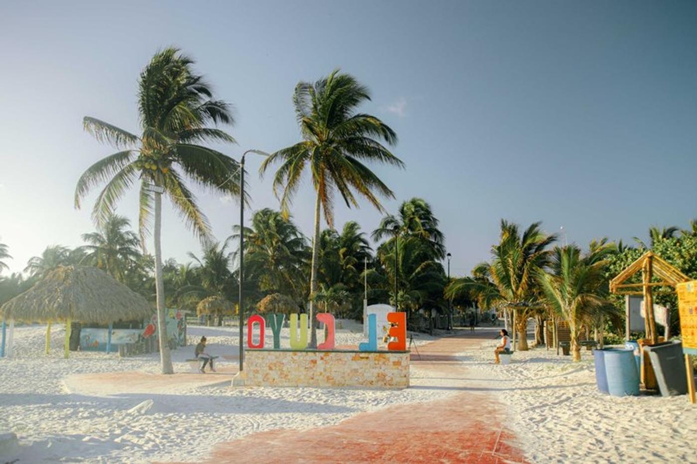 Plage bordée de palmiers à El Cuyo, Yucatan, avec des installations touristiques colorées et des cocotiers.
