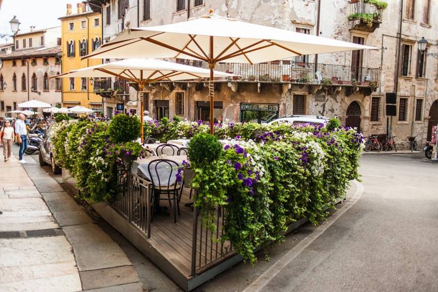 Terrasse fleurie dans une rue pittoresque de Vérone, entourée de bâtiments anciens et ornée de fleurs colorées.