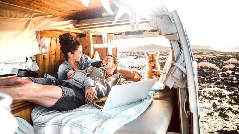 Couple de voyageurs nomades installés à l’arrière d’un van aménagé avec un ordinateur portable et leur chien, en pleine nature à Bordeaux.