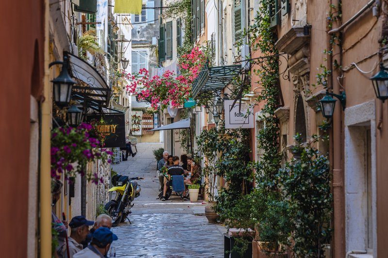 Ruelles étroites et fleuries de la vieille ville de Corfou, bordées de boutiques et de cafés locaux.