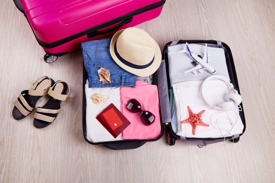 Valise ouverte contenant vêtements, accessoires et passeport, illustrant une préparation de voyage économique.