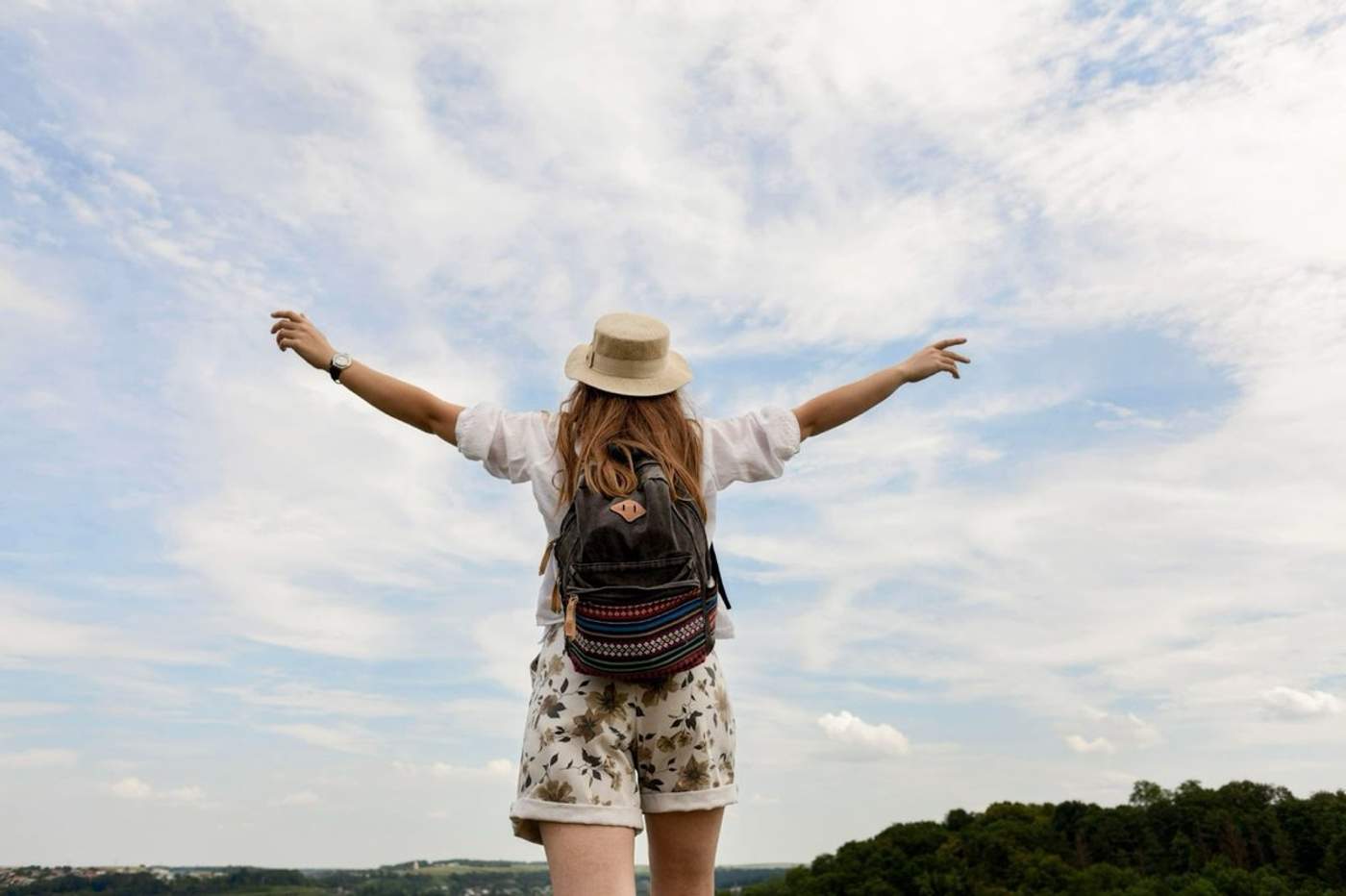 Voyageuse avec un chapeau et un sac à dos admirant la nature les bras ouverts, symbole de liberté et de voyage écoresponsable.