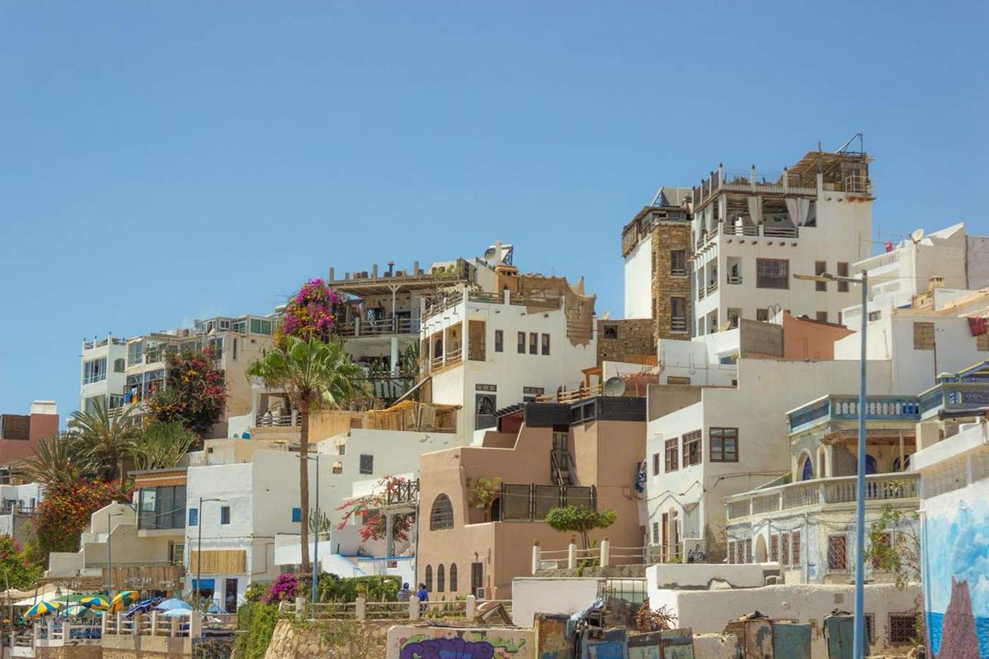 Façades blanches et ocres d'un quartier traditionnel d'Agadir, au Maroc, avec palmiers et bougainvilliers sous un ciel bleu.