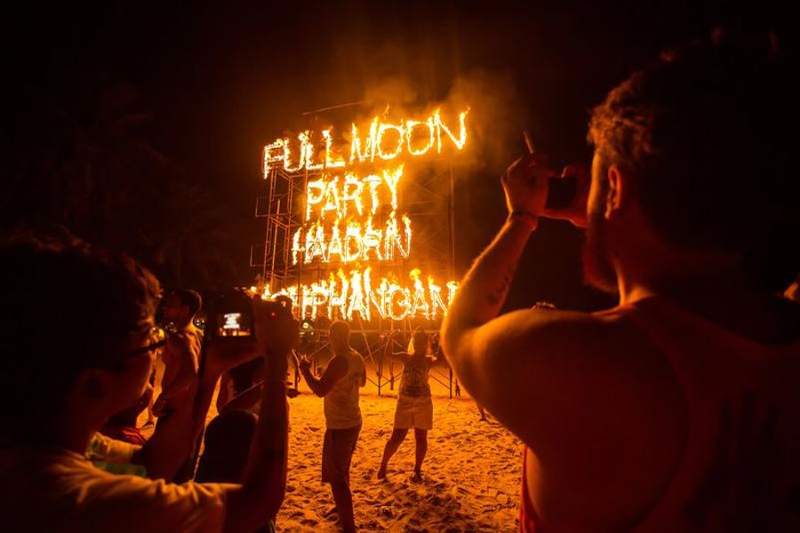 Enseigne enflammée indiquant “Full Moon Party” sur une plage animée de Koh Phangan.