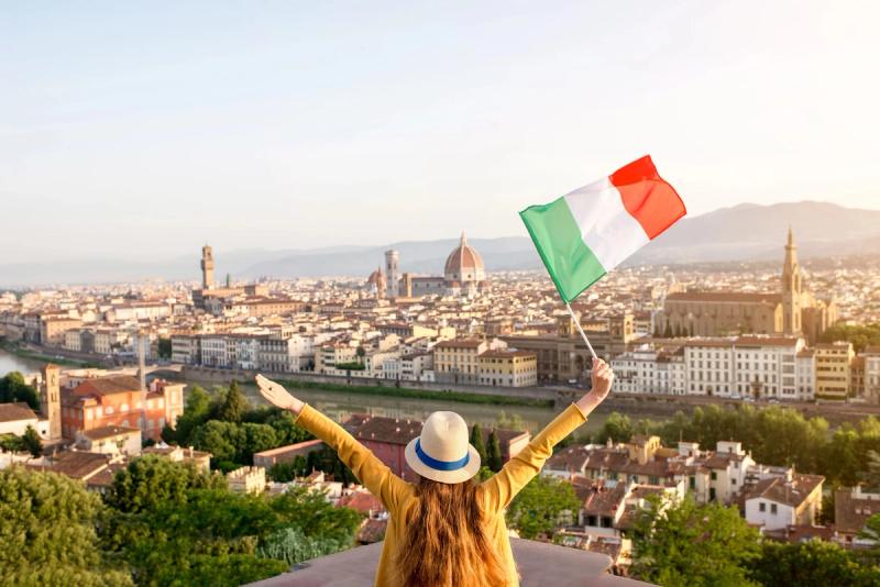 Une personne de dos, bras levés, brandissant un drapeau italien face à une vue panoramique de Florence, en Italie