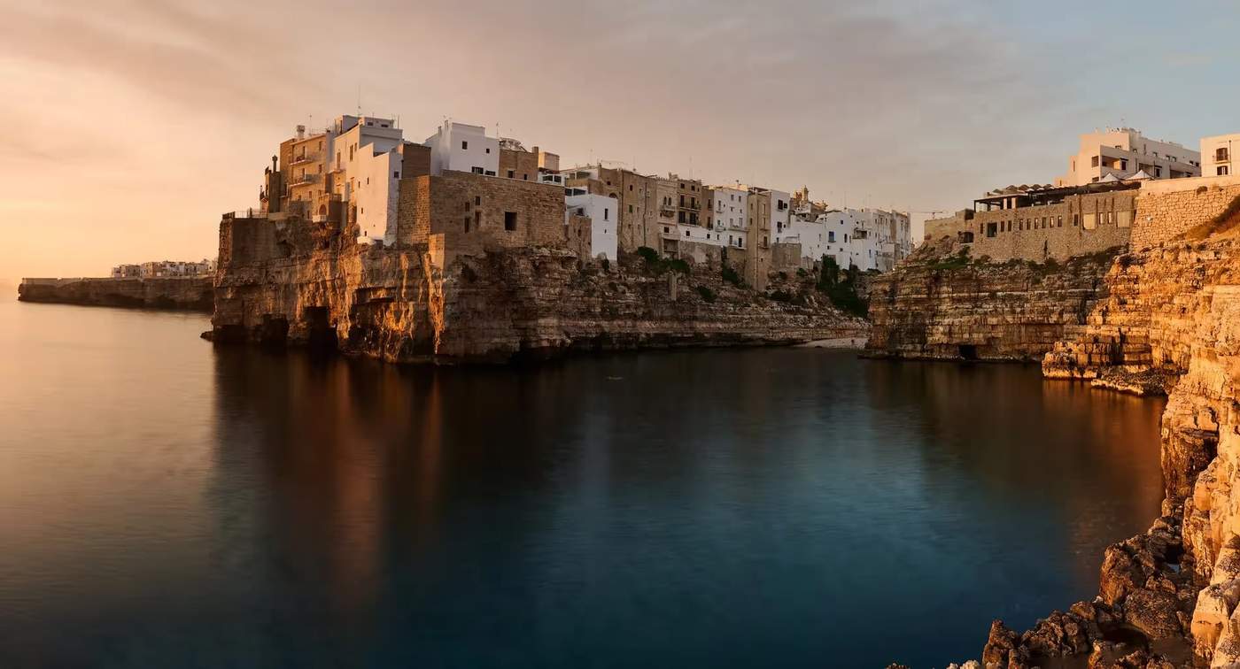 Vue sur Polignano a Mare au coucher du soleil, avec ses bâtiments en pierre surplombant la mer.