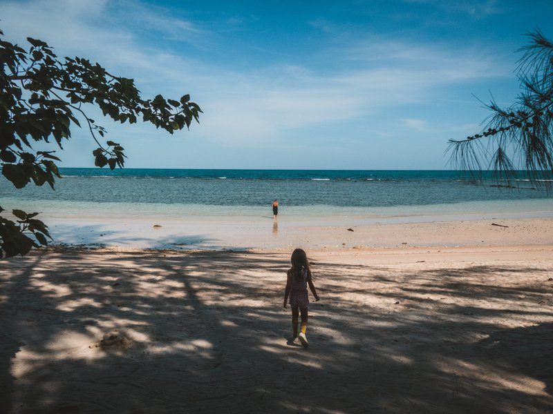 Anna marchant vers la mer sous un ciel bleu avec des arbres ombragés à Zen beach