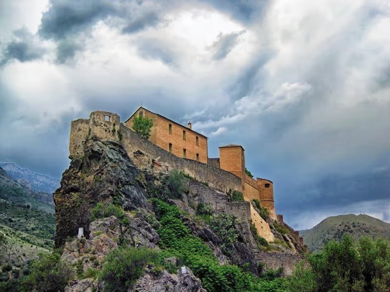 Citadelle perchée de Corte sous un ciel nuageux.