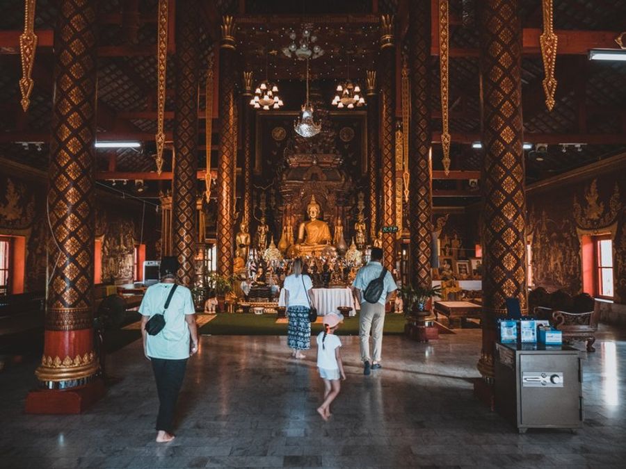 ntérieur d’un temple bouddhiste en Thaïlande avec une famille en visite devant une statue de Bouddha
