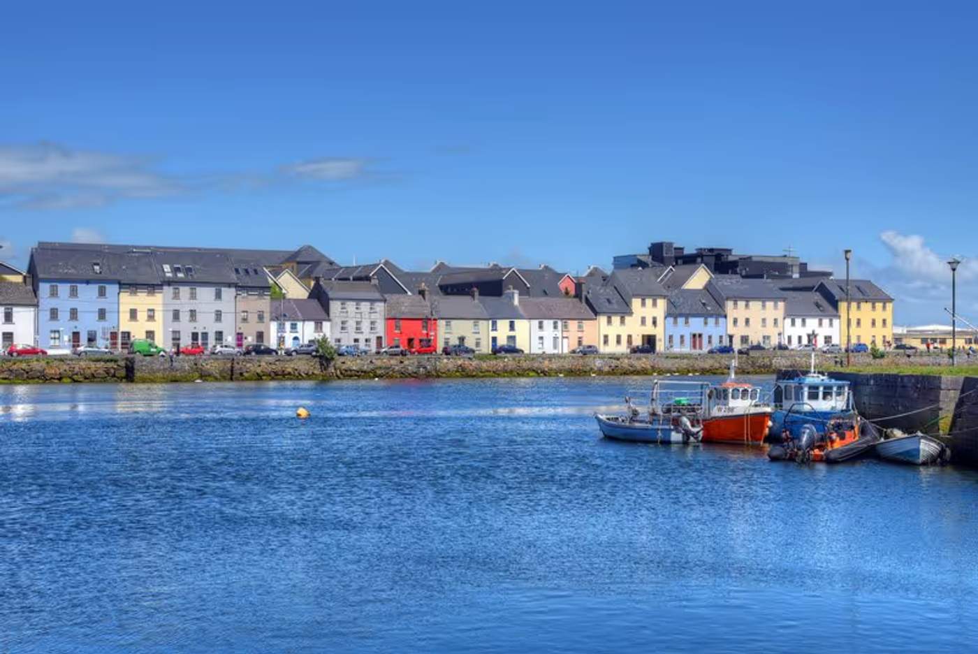 Le port de Galway avec des maisons colorées alignées le long du quai et des bateaux amarrés.