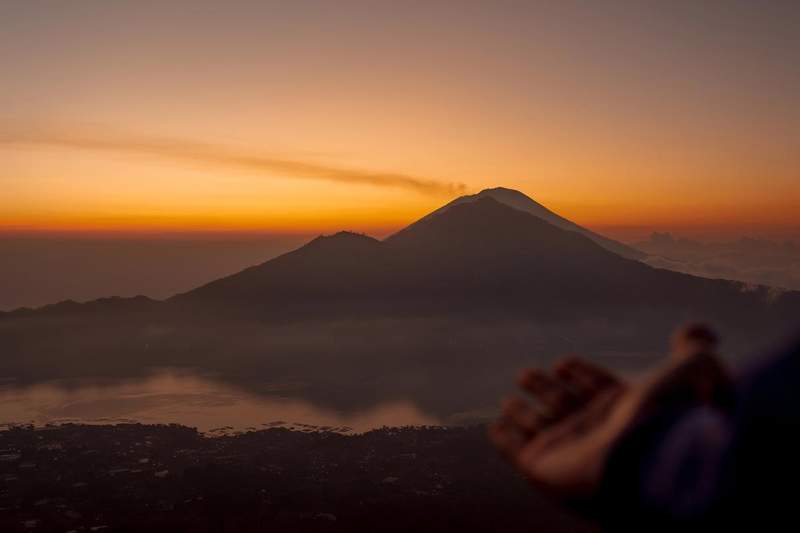Silhouette du mont Batur au lever du soleil, ciel orangé et lac Batur en arrière-plan, Bali