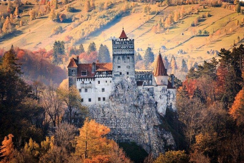 Château médiéval perché sur une colline, entouré de forêts, souvent associé à la légende de Dracula.