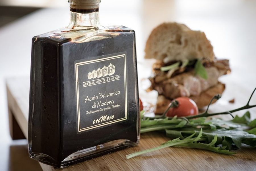Bouteille de vinaigre balsamique de Modène sur une table en bois avec un sandwich et une tomate en arrière-plan, Italie.