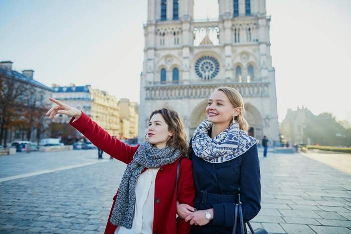 Deux femmes souriantes devant la cathédrale Notre-Dame à Paris, l’une pointant du doigt un monument à visiter.