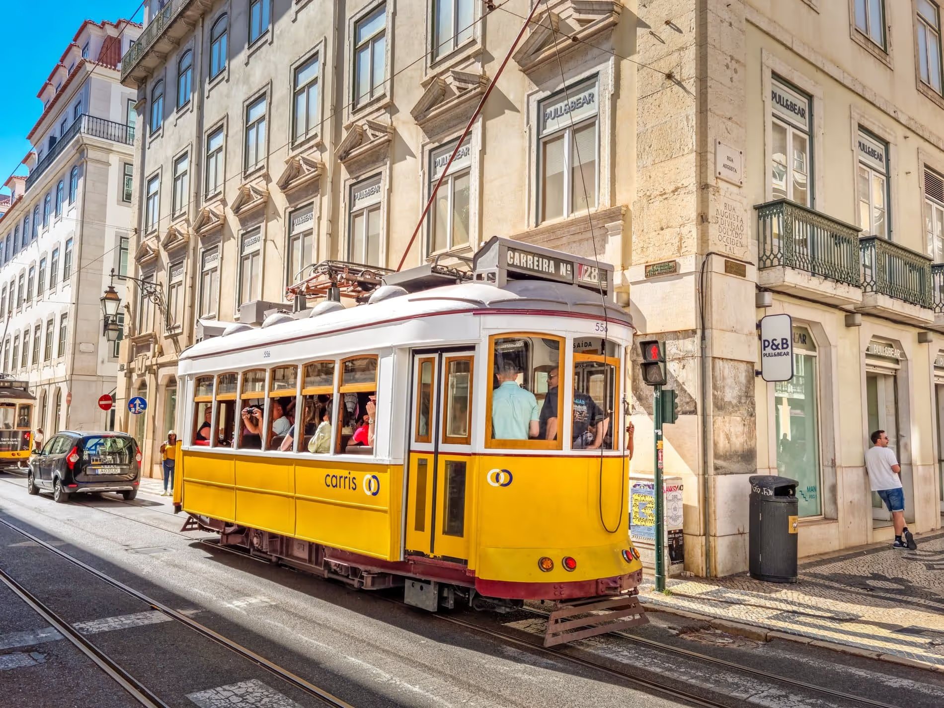Tramway jaune typique de Lisbonne passant dans une rue animée avec des bâtiments historiques en arrière-plan.