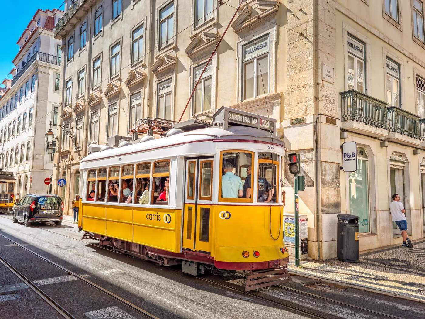 Tramway jaune typique de Lisbonne passant dans une rue animée avec des bâtiments historiques en arrière-plan.