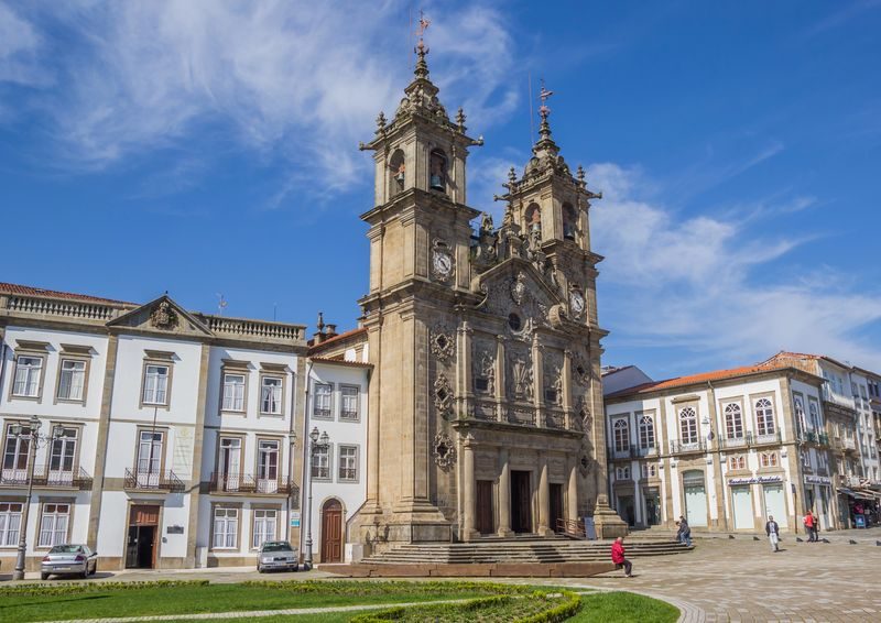 Façade ornée de l’église Santa Cruz à Braga, située sur une place lumineuse, avec un ciel bleu en arrière-plan.