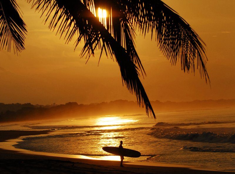 Coucher de soleil spectaculaire sur les plages de Nosara, avec un surfeur en contre-jour.