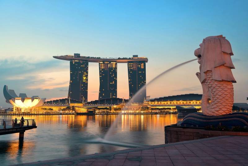 Vue emblématique de Singapour au crépuscule avec le Merlion crachant de l’eau et le Marina Bay Sands illuminé en arrière-plan.