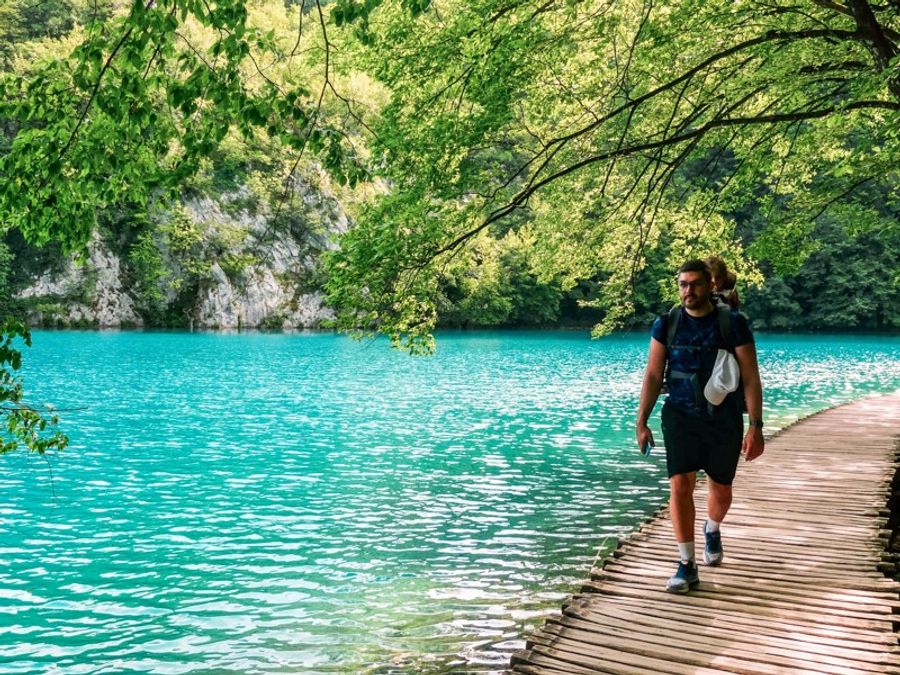 Homme marchant sur un ponton en bois au bord des lacs turquoise du parc national de Plitvice en Croatie.