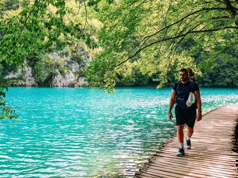 Homme marchant sur un ponton en bois au bord des lacs turquoise du parc national de Plitvice en Croatie.