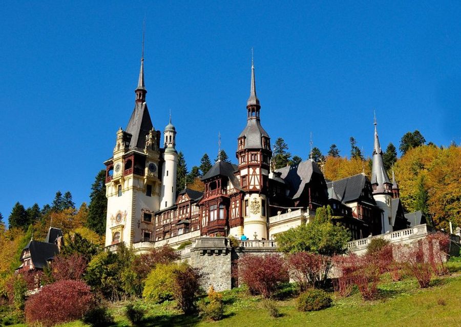 Le château de Peles en Transylvanie, entouré de collines verdoyantes, avec son architecture néo-Renaissance imposante et ses tours pointues.