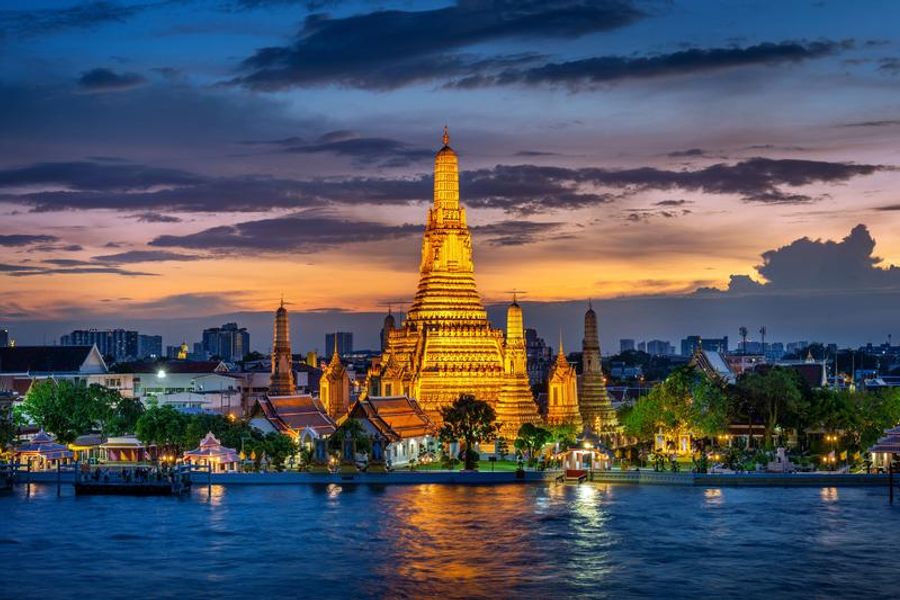 Temple Wat Arun illuminé au bord du fleuve Chao Phraya, avec un ciel de coucher de soleil.