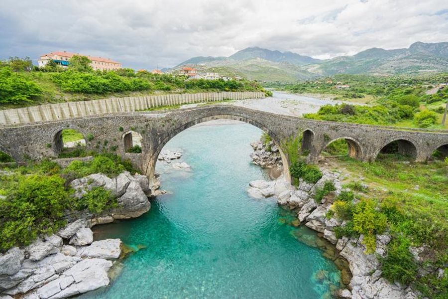 Vue sur le pont ottoman de Ura e Mesit à Shkodër, Albanie, enjambant une rivière turquoise entourée de nature verdoyante.