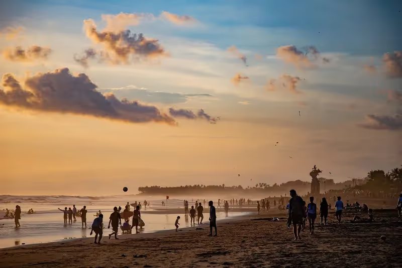 Scène de plage animée au coucher du soleil avec des gens qui marchent, jouent et profitent de la vue.
