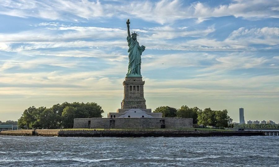 La Statue de la Liberté se dressant majestueusement sur Liberty Island sous un ciel partiellement nuageux.