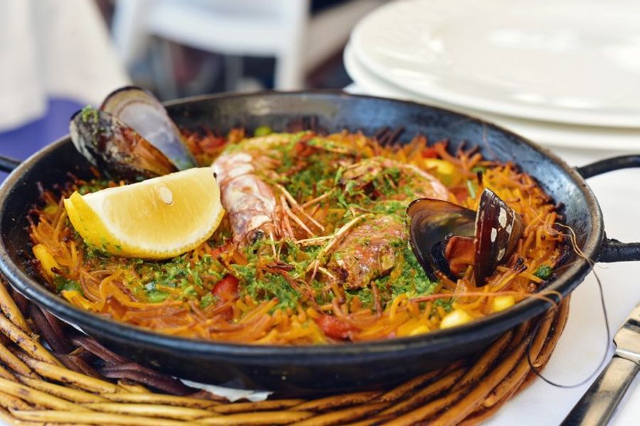 Une fideuà traditionnelle servie dans une poêle, avec des fruits de mer, des nouilles et une tranche de citron.