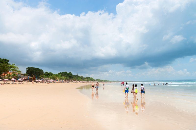 Promeneurs le long de la plage de Seminyak, Bali, sous un ciel partiellement nuageux.