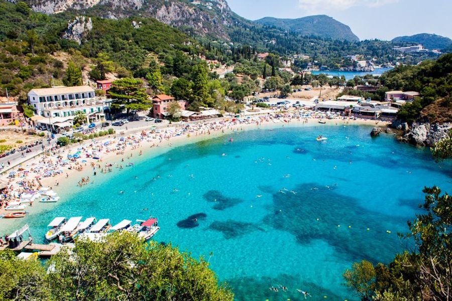 Plage animée à Corfou avec des eaux turquoise et des bateaux de plaisance.