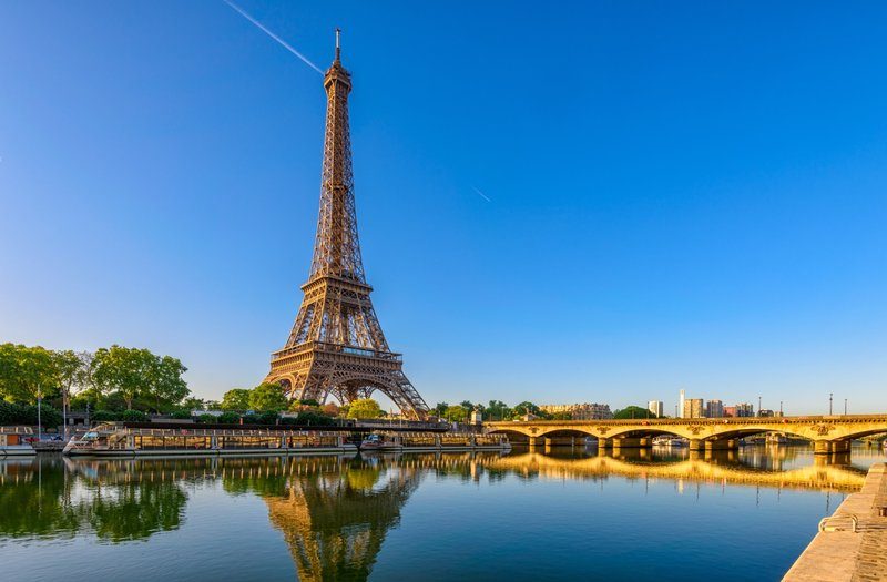 La tour Eiffel se reflétant dans la Seine par temps clair, avec un pont parisien au premier plan.