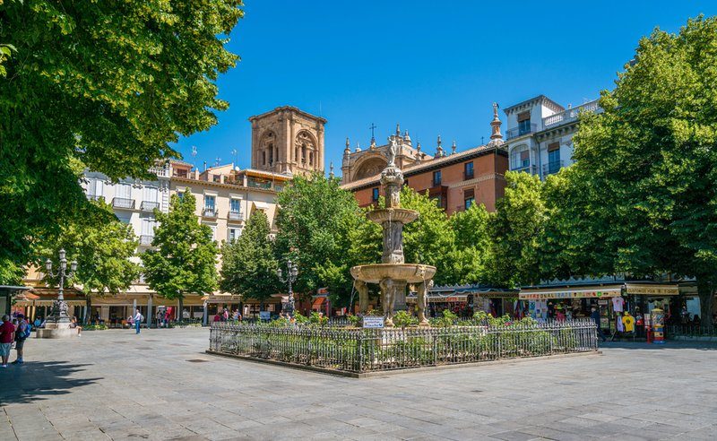 Vue sur la Plaza Bib-Rambla à Grenade avec sa fontaine et ses arbres verdoyants en arrière-plan.