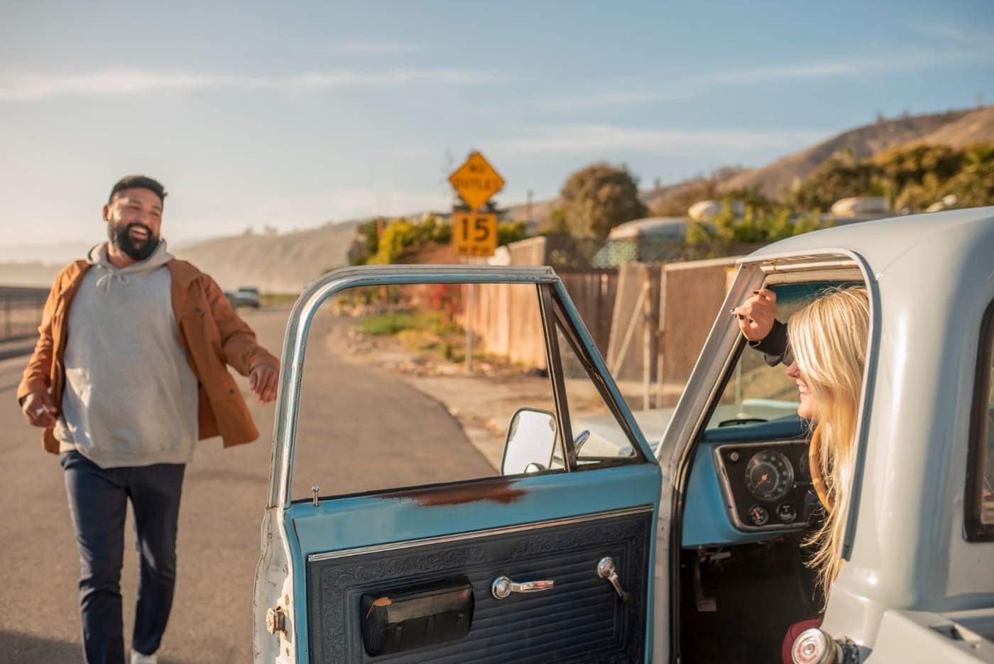 Couple souriant à côté d'un pick-up vintage bleu et blanc sur une route de bord de mer