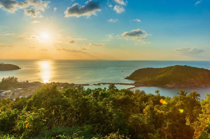 Vue panoramique d'un coucher de soleil sur une baie tropicale entourée de végétation luxuriante et d'une petite île verdoyante en Martinique.