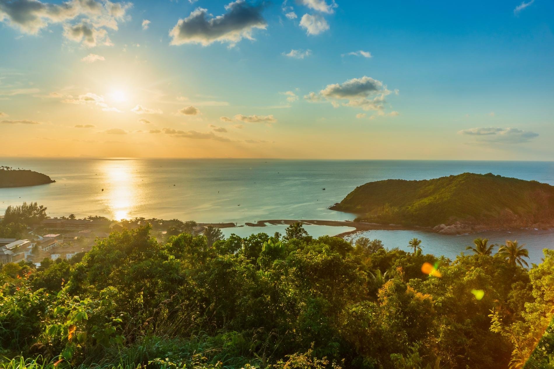 Vue panoramique d'un coucher de soleil sur une baie tropicale entourée de végétation luxuriante et d'une petite île verdoyante en Martinique.