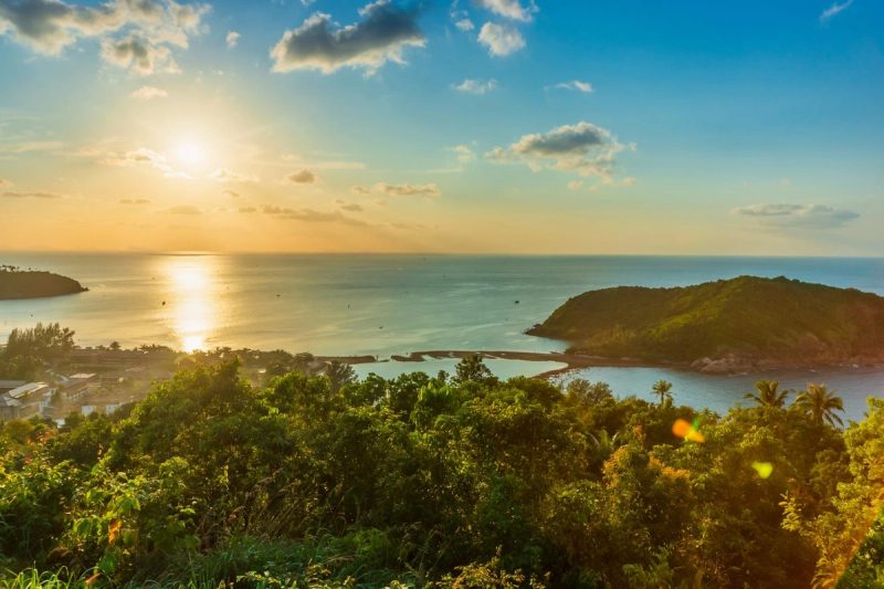 Vue panoramique d'un coucher de soleil sur une baie tropicale entourée de végétation luxuriante et d'une petite île verdoyante en Martinique.