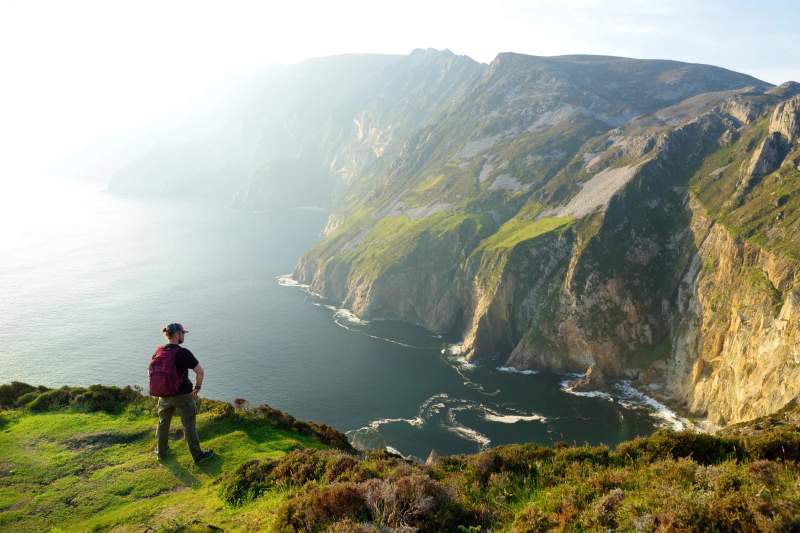 Un randonneur contemplant les falaises spectaculaires et les vues sur l'océan Atlantique depuis une hauteur en Irlande, illustrant la beauté naturelle et sauvage du pays.