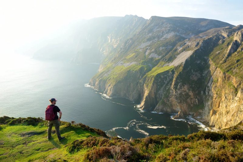 Un randonneur contemplant les falaises spectaculaires et les vues sur l'océan Atlantique depuis une hauteur en Irlande, illustrant la beauté naturelle et sauvage du pays.