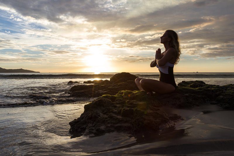 Femme pratiquant le yoga au coucher du soleil sur une plage paisible de Nosara, Costa Rica.