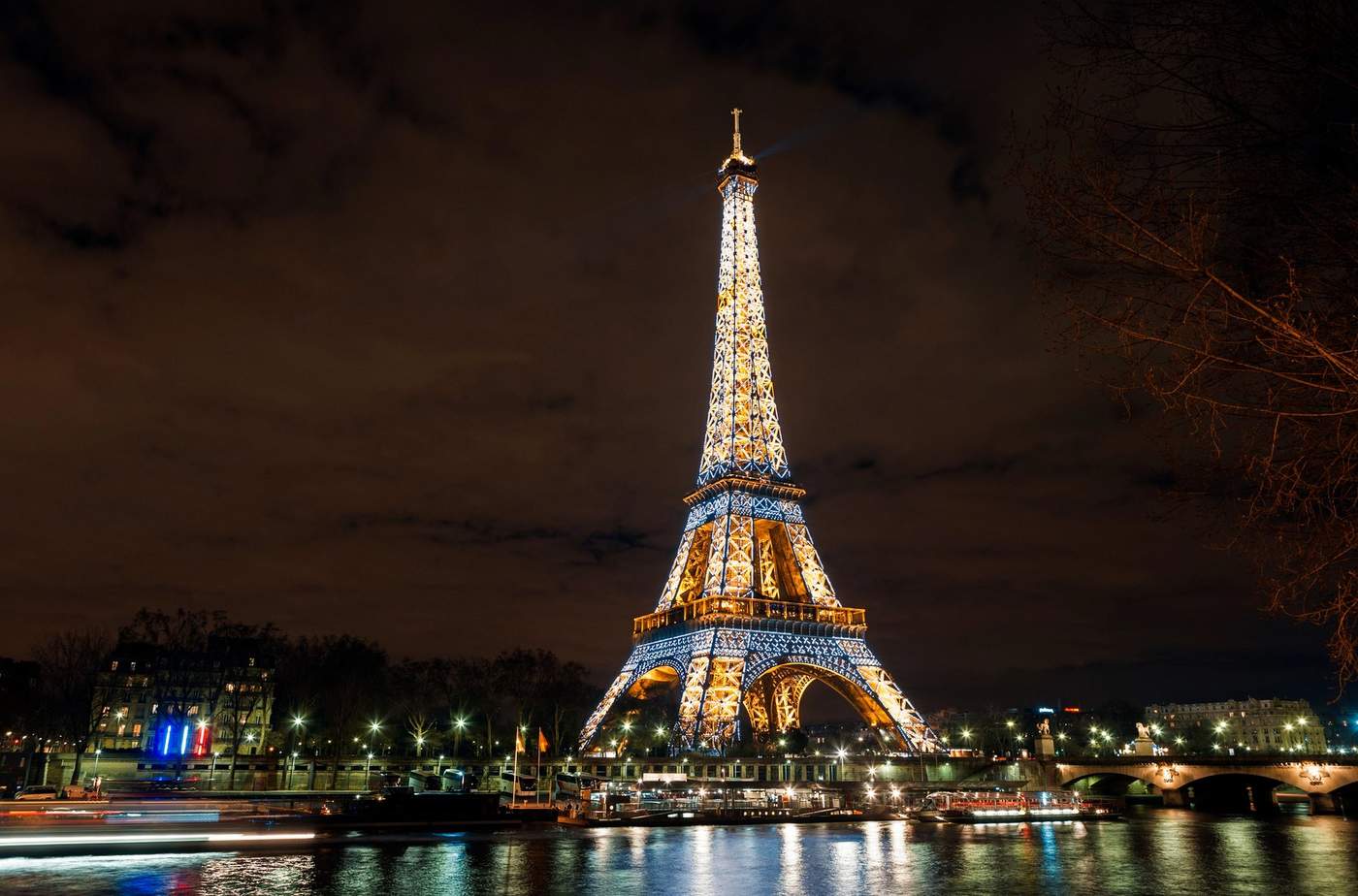 Vue nocturne spectaculaire de la tour Eiffel illuminée, se reflétant dans la Seine à Paris.