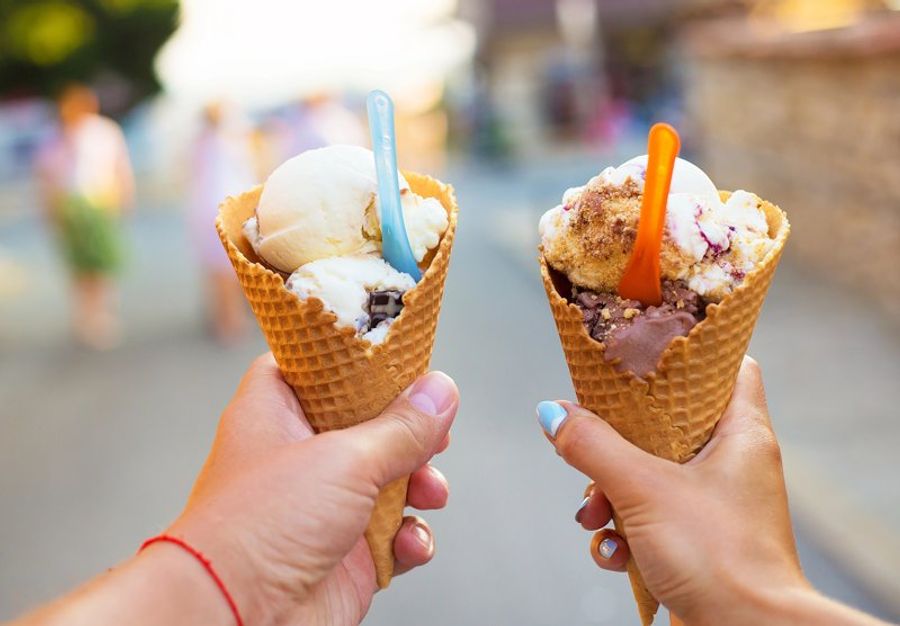 Deux cornets de glace appétissants, tenus par des mains, avec des saveurs variées et des cuillères colorées.