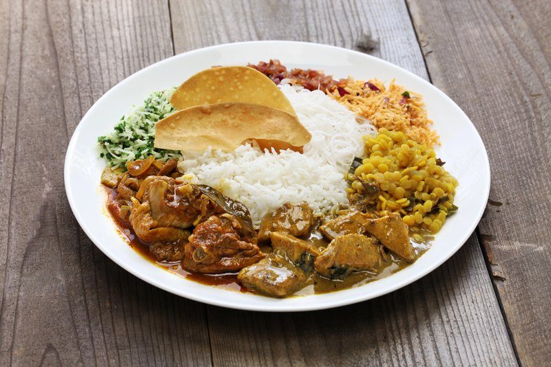 Assiette de curry sri-lankais composée de riz, lentilles jaunes, nouilles de riz, légumes, et morceaux de viande en sauce avec des papadums.