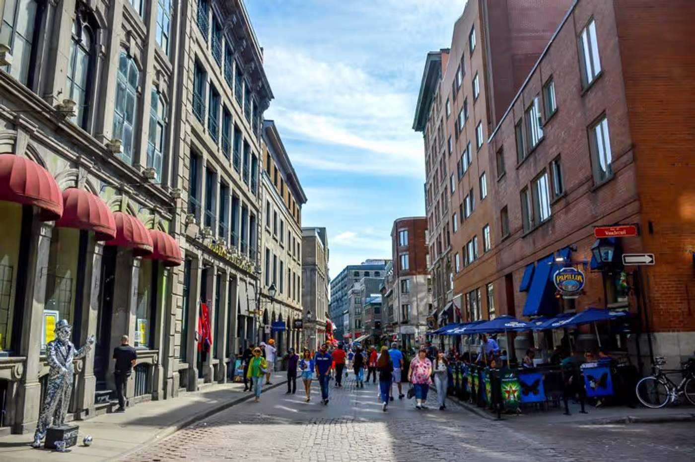 Une rue animée du Vieux-Montréal, avec des bâtiments en pierre, des terrasses et des piétons.